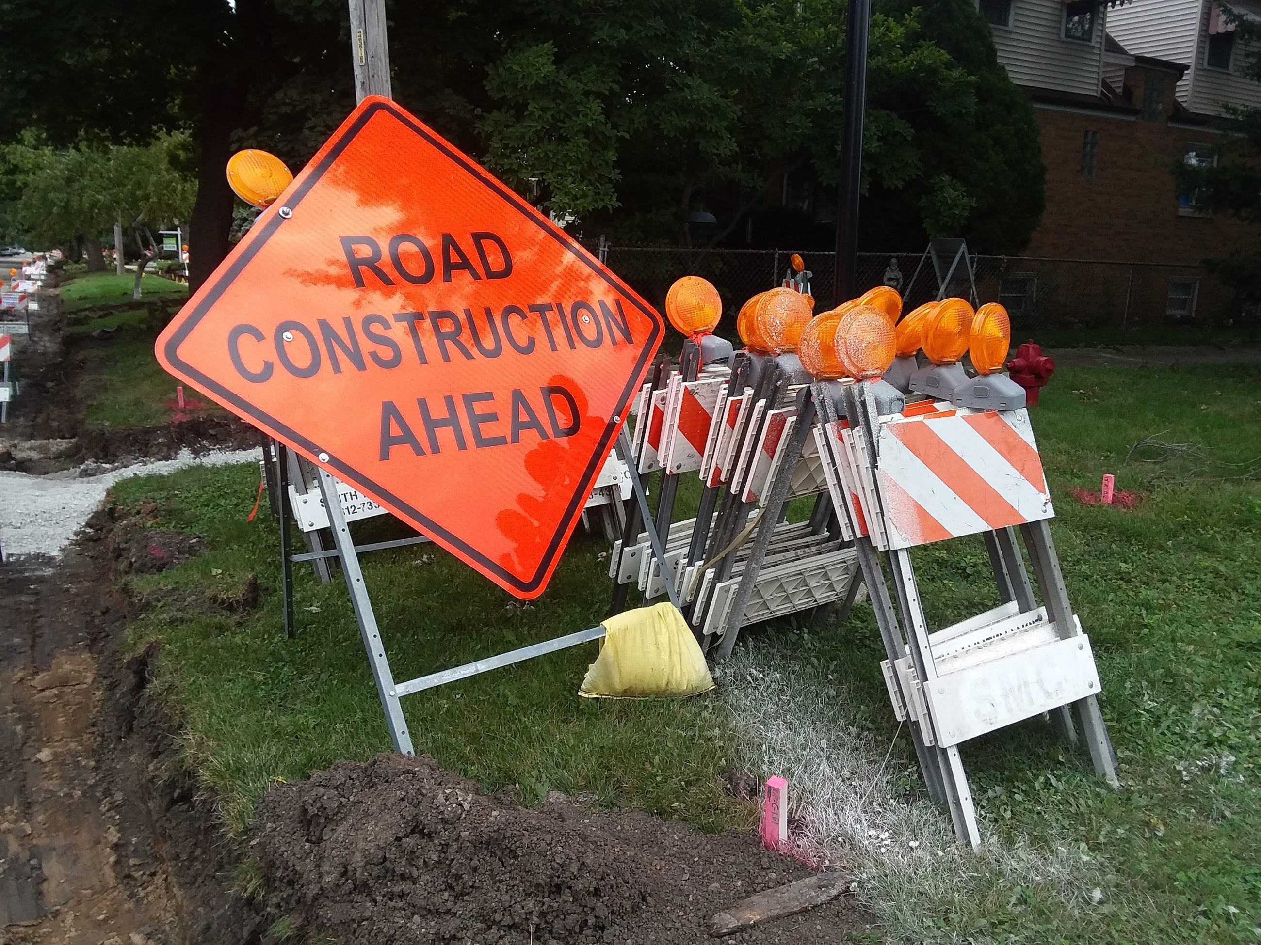Orange Road Construction sign next to orange and white barricades